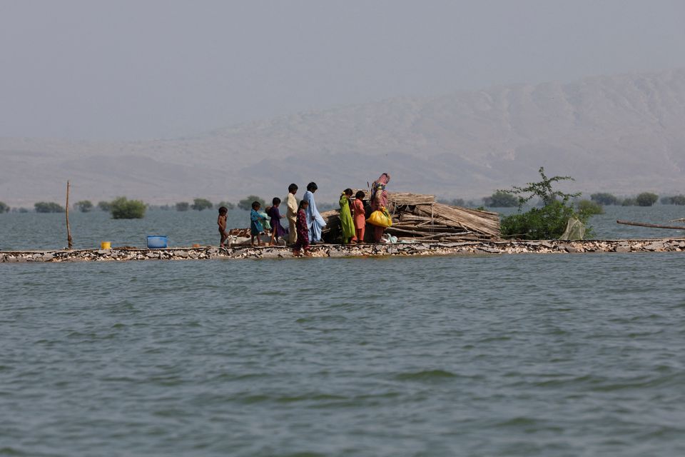 A woman and children walk as they take refuge along a damaged road amid flood, following rains and floods during the monsoon season in Bajara village, at the banks of Manchar lake, in Sehwan, Pakistan 6 September 2022. Photo: Akhtar Soomro / REUTERS