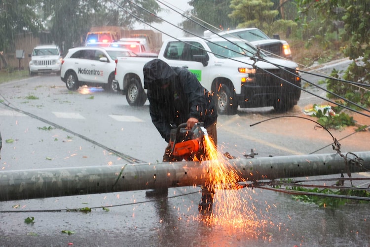 A worker cuts an electricity pole knocked down by Hurricane Fiona and blocking a road in Cayey de Muesas, Puerto Rico on 18 September 2022. Photo: Stephanie Rojas / AP