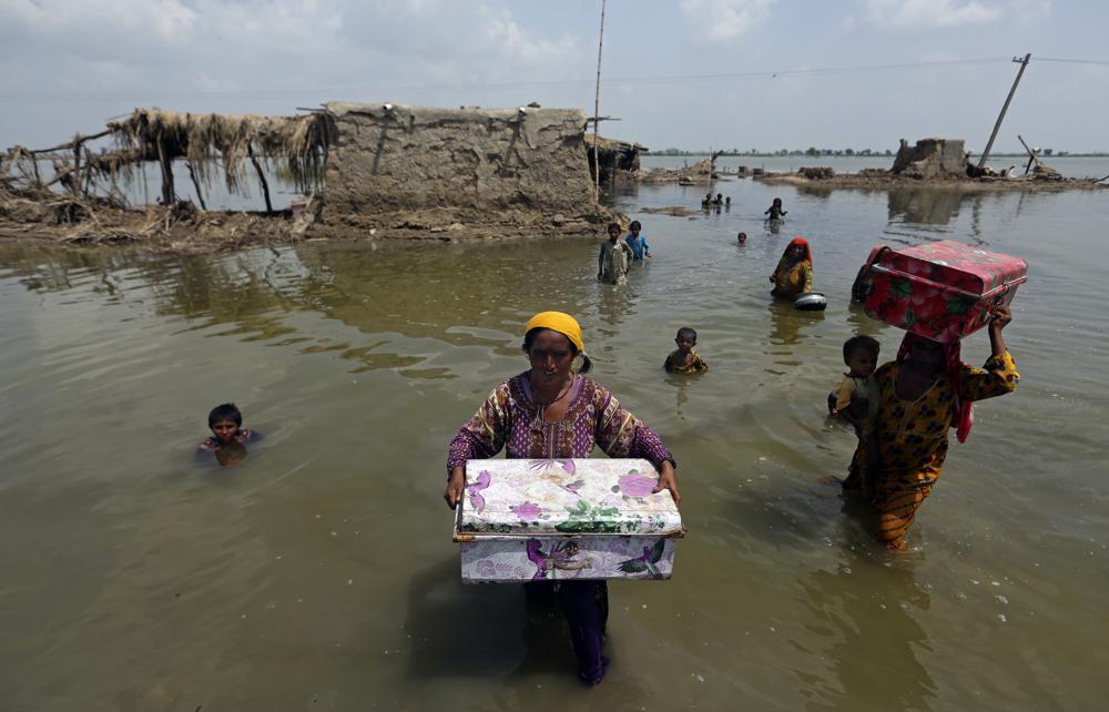 Women carry belongings salvaged from their flooded home after monsoon rains, in the Qambar Shahdadkot district of Sindh Province, of Pakistan, 6 September 2022. The war in Ukraine, the lingering coronavirus pandemic and climate change are putting intense pressure on the world's poorest, the Organization for Economic Cooperation and Development warned. Photo: Fareed Khan / AP Photo