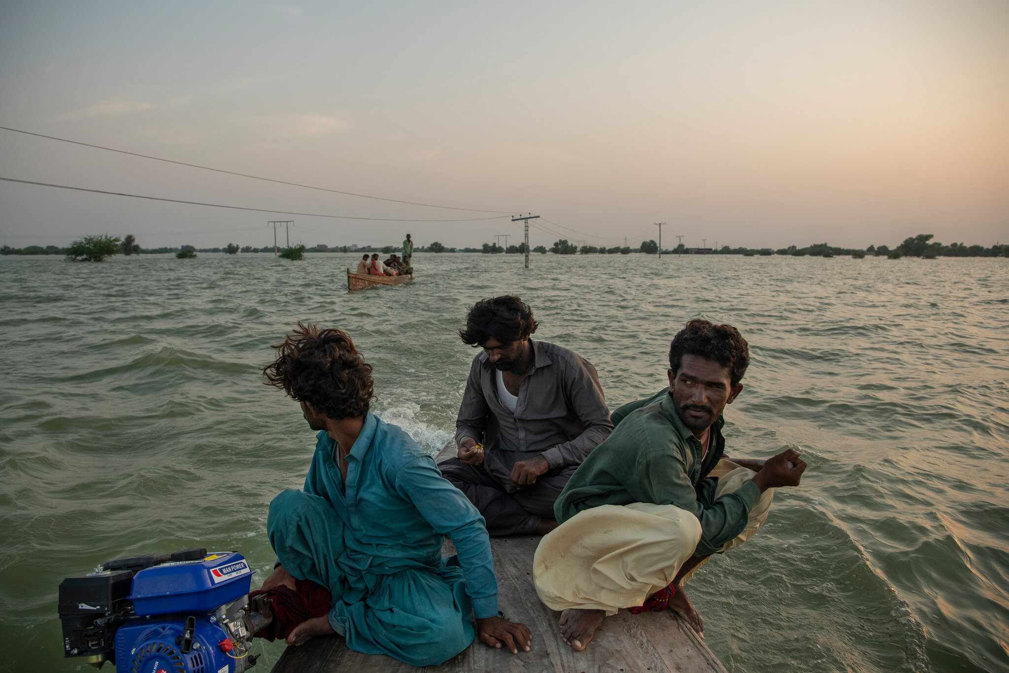 Boat operators, who have come from miles around to work as ferrymen in submerged areas, use power lines as navigation landmarks in Dadu, Pakistan, on Tuesday, 13 September 2022. They have become a lifeline for residents who are trying to save the livestock and belongings that were not washed away by floodwaters. Photo: Kiana Hayeri / The New York Times