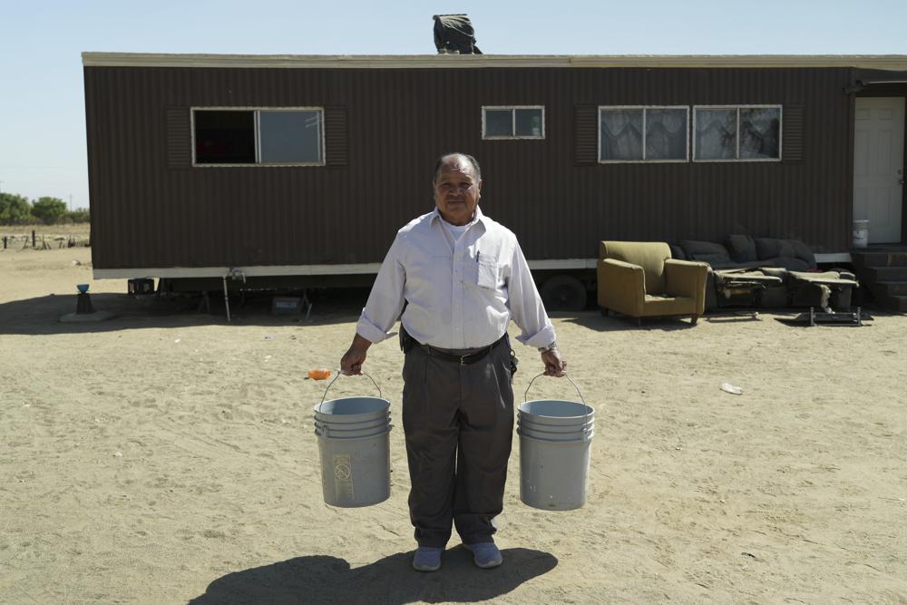 Tomas Chairez carries the buckets his tenants use to carry water from a neighbor's home because his property lost access to groundwater in Fairmead, California, 14 September 2022. Chairez is trying to get the county to provide a storage tank and water delivery service. For now, his tenants have to fill up 5-gallon (19-liter) buckets at a friend’s home and transport water by car each day. Photo: AP Photo / Terry Chea