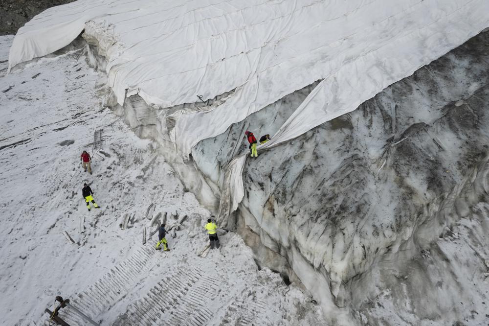 People work on a tarpaulin which cover the ice of the Corvatsch glacier, near Samedan, Switzerland, 5 September 2022. Glaciologists have stopped their program to measure the glacier. The decision has already been taken in 2019 and the hot summer of 2022 has led to extreme losses of ice” and the end of the program. The covered part of the glacier is used as a ski slope in winter. Photo: Gian Ehrenzeller / Keystone / AP
