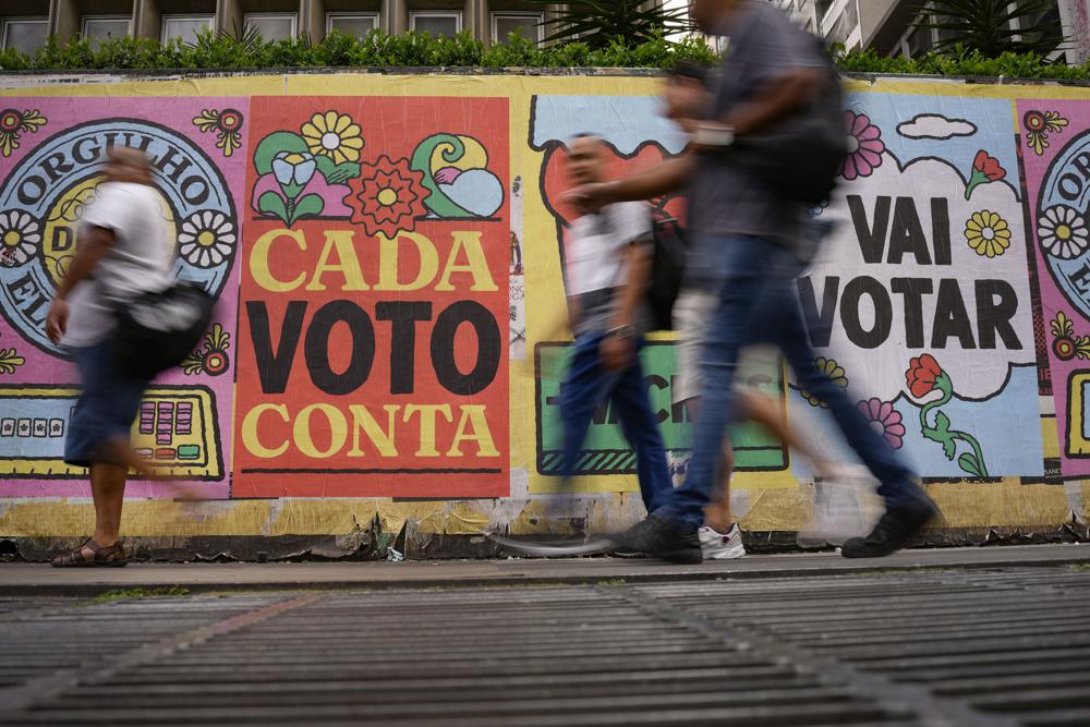People walk past a mural that reads in Portuguese: “Every vote counts” in Sao Paulo, Brazil, 25 October 2022. In a last-minute effort to win reelection on Sunday, 30 October, Marcos Rocha, the governor of Rondonia, in the Brazilian Amazon and a staunch ally of far-right President Jair Bolsonaro, revoked the protection of a large swath of the Amazon forest. Photo: Matias Delacroix / AP Photo