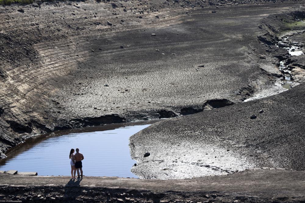 A couple stands on what was an ancient packhorse bridge exposed by low water levels at Baitings Reservoir in Yorkshire as record high temperatures hit Ripponden, England, 12 August 2022. Widespread drought that dried up large parts of Europe, the United States and China this past summer was made 20 times more likely by climate change, according to a new study. Photo: Jon Super / AP Photo