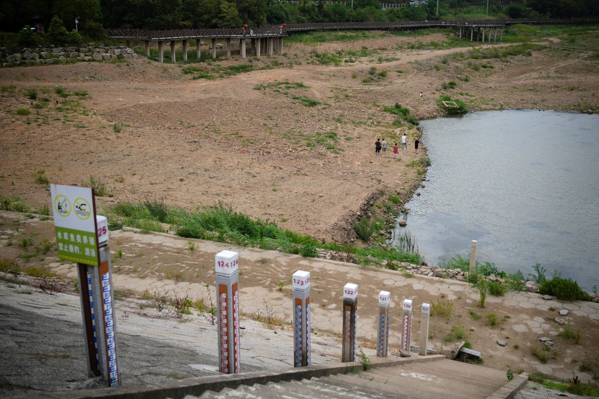 A family walks on a dried-up bed of a reservoir as water level poles emerge after waters receded, amid hot temperatures, while many regions from southwest to east of the country along the Yangtze River experienced weeks of record-breaking heatwave in Changxing, Zhejiang province, China, 20 August 2022. Photo: Aly Song / REUTERS