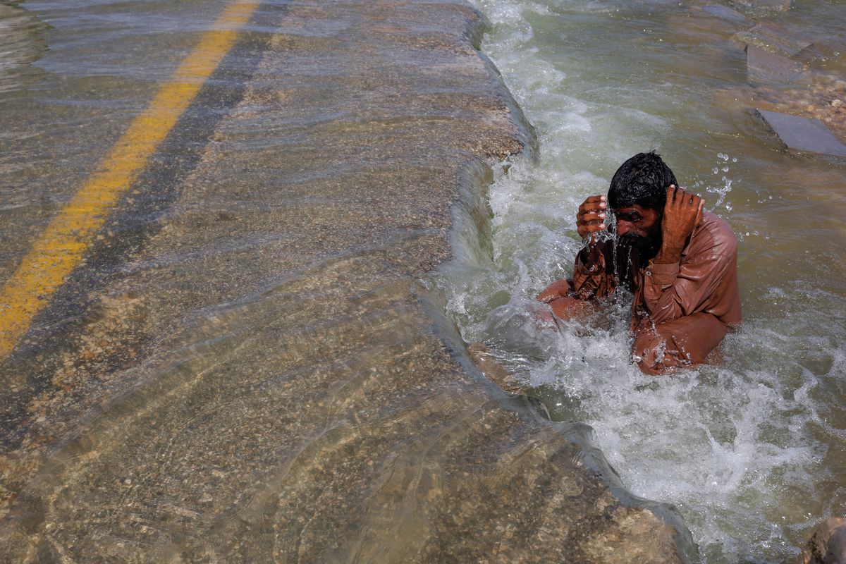 A displaced man cools off to avoid heat on flooded highway, following rains and floods during the monsoon season in Sehwan, Pakistan, 16 September 2022. Photo: Akhtar Soomro / REUTERS