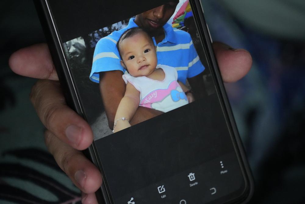 Hyancinth Charm Garing shows a picture of her husband Jeremy with their year-old baby daughter Hywin during an interview in their home at a new community for victims of super Typhoon Haiyan in Tacloban, central Philippines on Sunday, 23 October 2022. Garing and his family settled at a relocation site for victims of super Typhoon Haiyan after their village was wiped out when it struck in 2013, killing six family members and their daughter Hywin. Photo: Aaron Favila / AP Photo