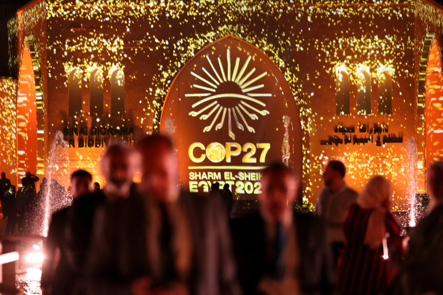 People pass in front of a wall lit with the sign of COP27 as the COP27 climate summit takes place, at the Green Zone in Sharm el-Sheikh, Egypt, 10 November 2022. Photo: REUTERS