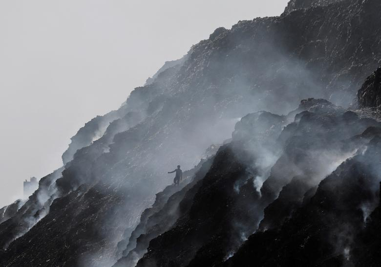 A waste collector climbs down while looking for recyclable materials as smoke billows from burning garbage at the Bhalswa landfill site on World Environment Day in New Delhi, India, 5 June 2022. Photo: Anushree Fadnavis / REUTERS