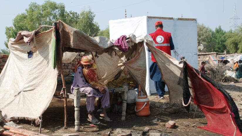A woman affected by intense flooding in Pakistan in 2022 sits in her makeshift shelter while Pakistan Red Crescent Society volunteers work hard to improve shelter and health conditions in his community. Photo: Angbeen Sohail / IFRC