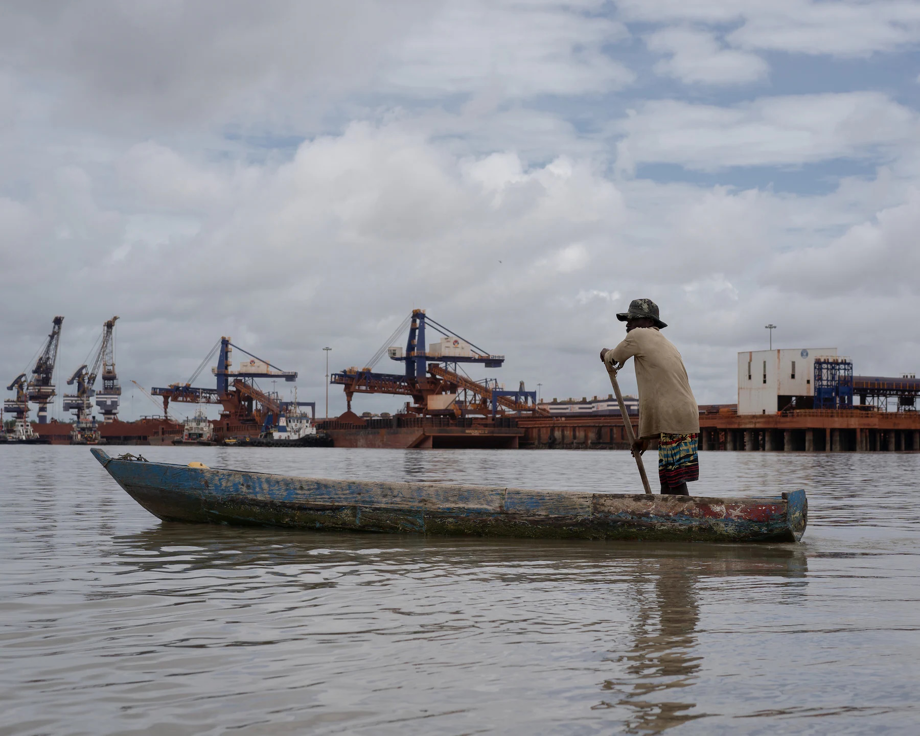 A fisherman passes near a mining port in Guinea. The presence of the port and container ships has considerably reduced the quantity of fish. Fisherman Aboubacar Camara says that his daily catch has greatly decreased and that SMB's security patrol speedboats routinely slash fishermen's nets as they pass by. Photo: Chloe Sharrock / MYOP / The Washington Post