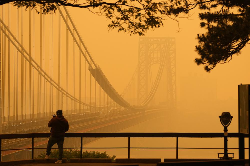 A man talks on his phone as he looks through the haze at the George Washington Bridge from Fort Lee, N.J., Wednesday, 7 June 2023. Intense Canadian wildfires are blanketing the northeastern U.S. in a dystopian haze, turning the air acrid, the sky yellowish gray and prompting warnings for vulnerable populations to stay inside. Photo: Seth Wenig / AP Photo