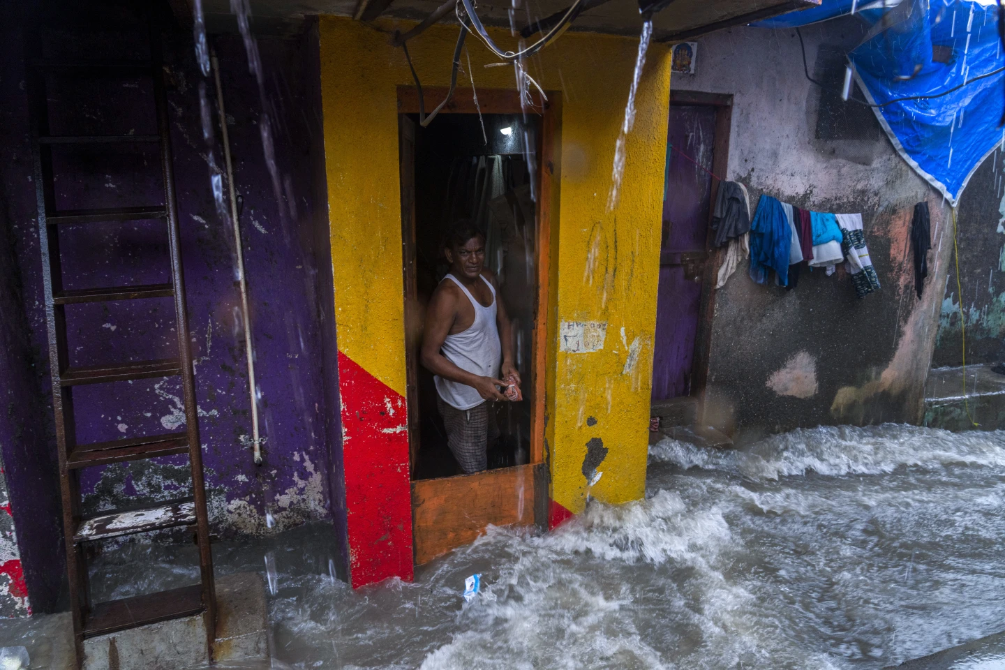 An Indian man stands at the door of his house as waves caused by high tide hits the huts on the shore of the Arabian Sea in Mumbai, India, Thursday, 6 July 2023. Photo: Rafiq Maqbool / AP Photo
