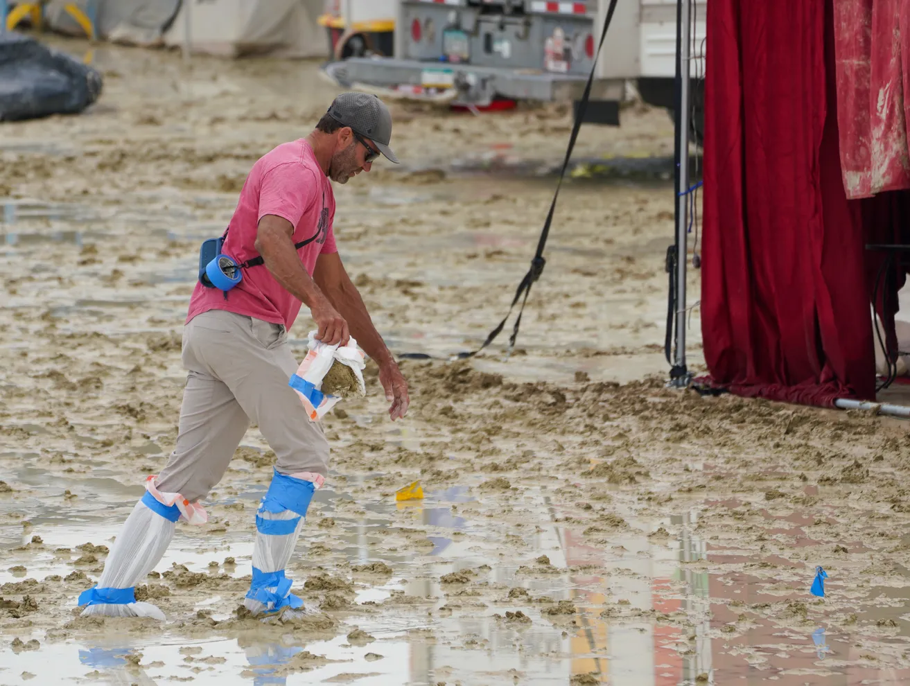 A Burning Man participant wearing plastic bags taped over his feet trudges through the mud in Black Rock City, in the Nevada desert, after a rainstorm flooded the site and stranded thousands, 2 September 2023. Photo: Trevor Hughes / USA TODAY