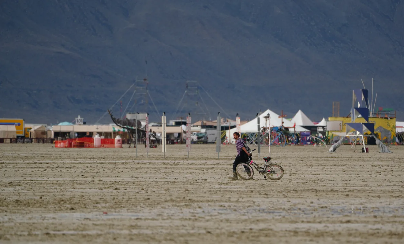 A man trudges through mud at the flooded Burning Man festival on 2 September 2023, dragging a bicycle made useless by the morass after a rainstorm flooded the site and stranded thousands Photo: Trevor Hughes / USA TODAY