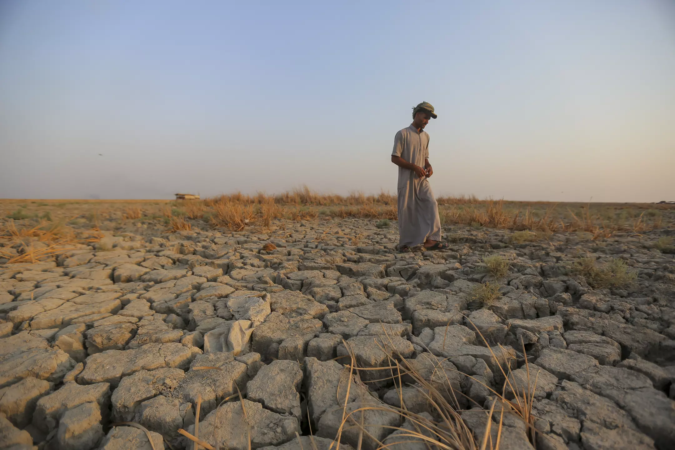 A fisherman walks across a dry patch of land in the marshes in Dhi Qar province, Iraq, during a severe drought in 2022. Photo: Anmar Khalil / Associated Press