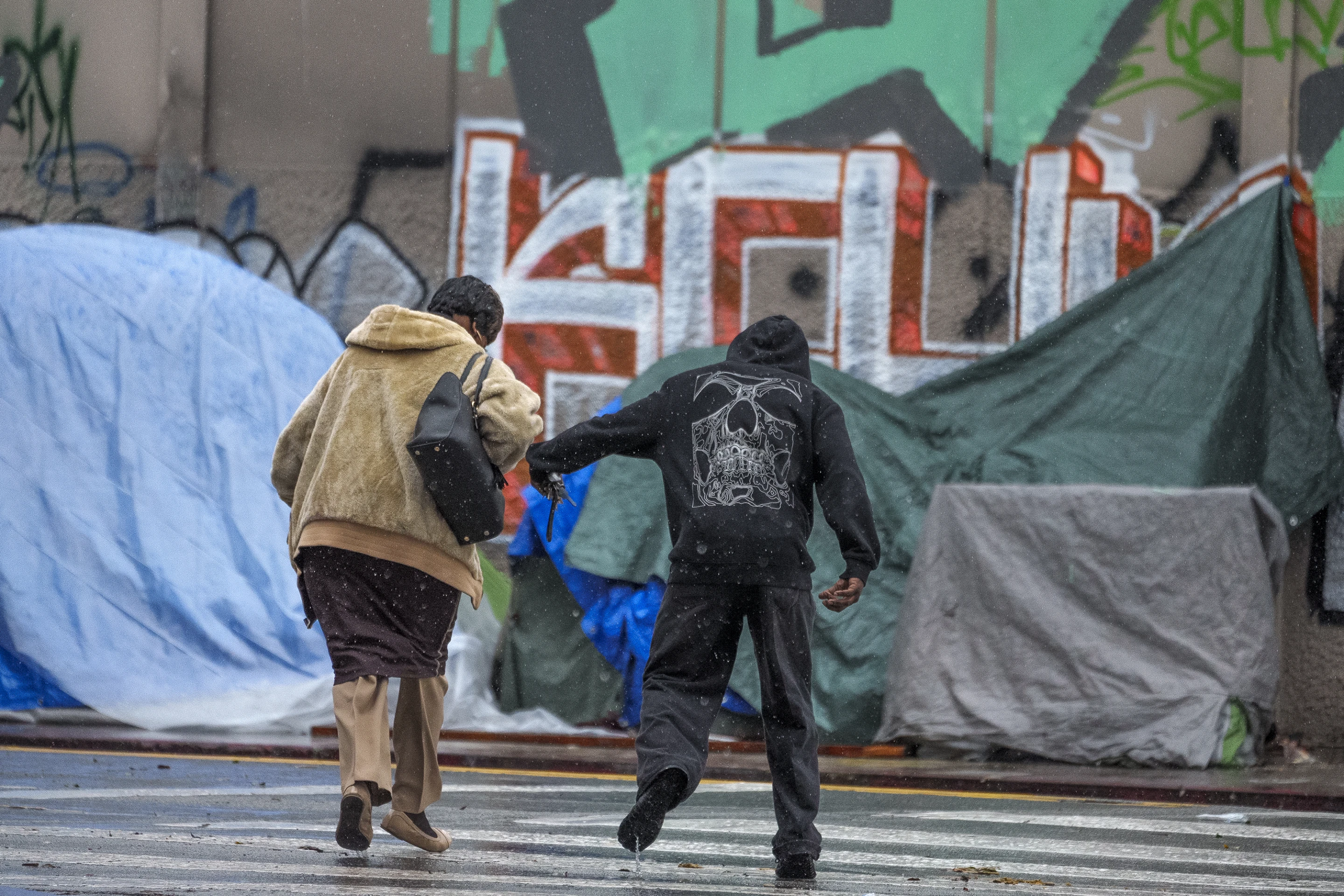 People cross the street under heavy rain in the Skid Row area, one of the largest populations of homeless people in the United States, Monday, 5 February 2024, in Los Angeles. A storm of historic proportions dumped a record amount of rain over parts of Los Angeles on Monday, sending mud and boulders down hillsides dotted with multimillion-dollar homes while people living in homeless encampments in many parts of the city scrambled for safety. Shelters were adding beds for the city’s homeless population of nearly 75,000 people. Photo: Damian Dovarganes / AP Photo