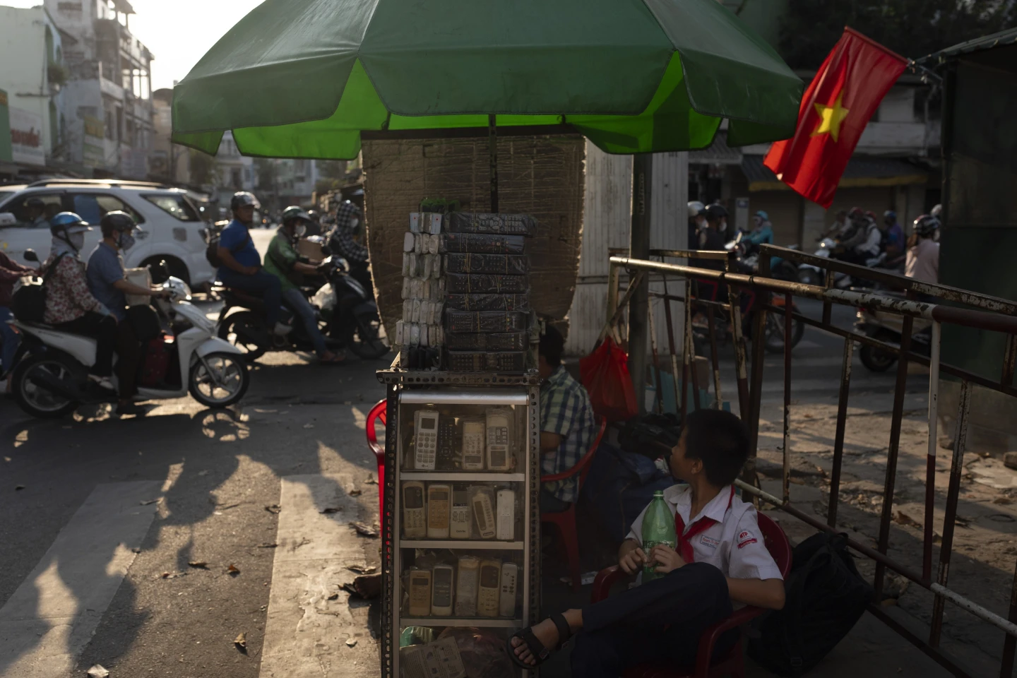 A boy in a school uniform sits next to a vendor selling used remote controls for various home appliances in Nhat Tao market, the largest informal recycling market in Ho Chi Minh City, Vietnam, Wednesday, 31 January 2024. Photo: Jae C. Hong / AP Photo