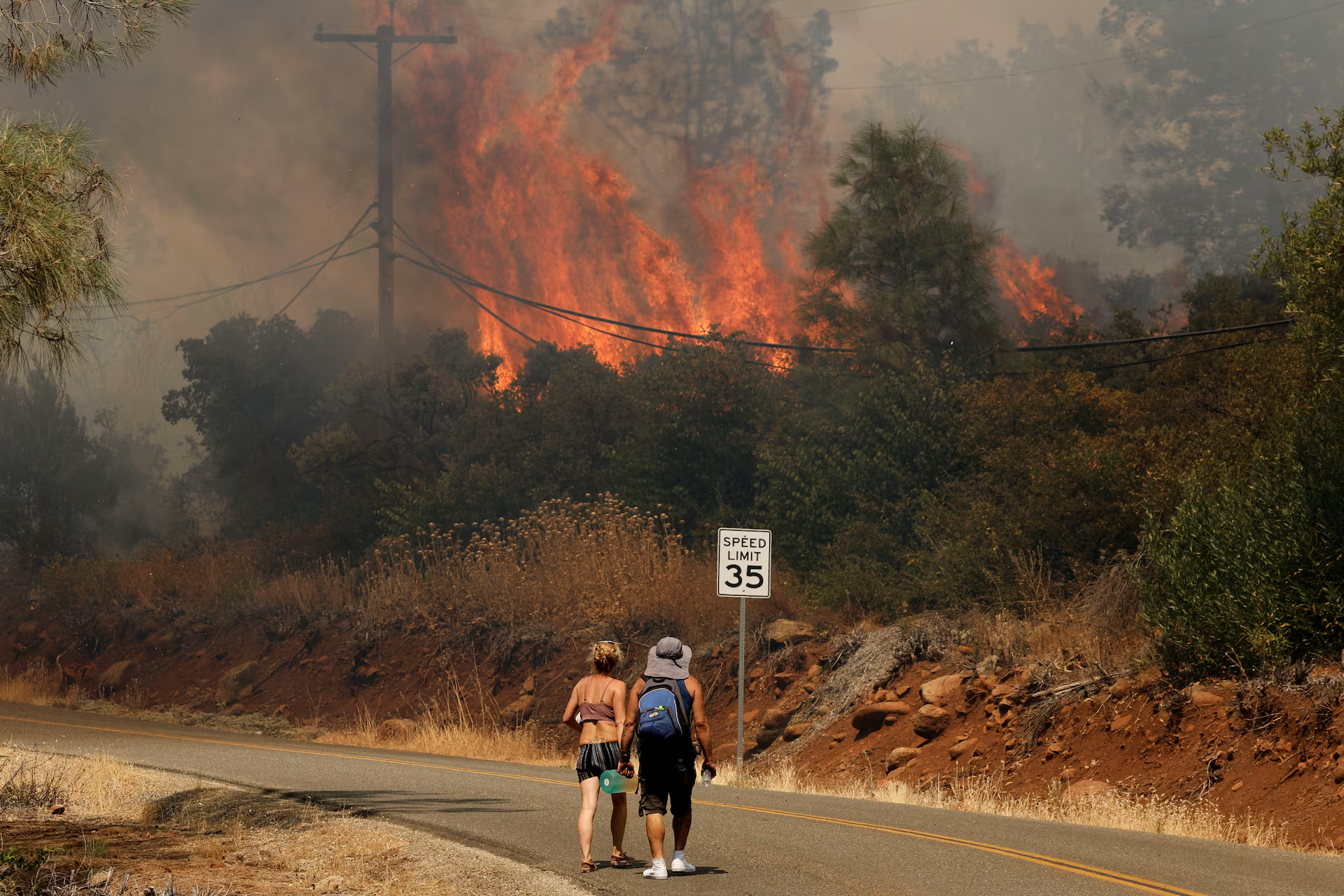 People walk on the road near flames and smoke plume rising as firefighters continue to tackle the Park Fire near the northern Sacramento Valley city of Chico, California, U.S. 25 July 2024. Photo: Fred Greaves / REUTERS