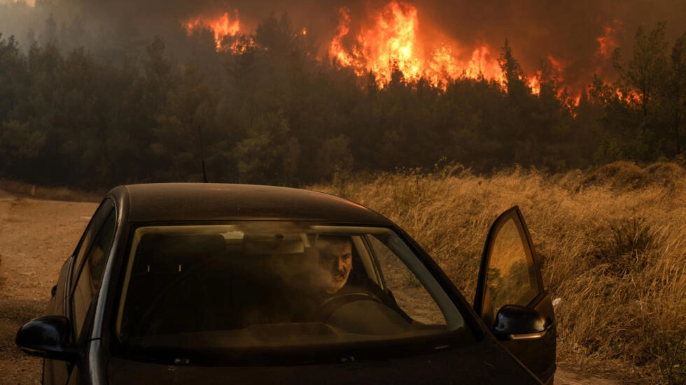 A man gets in his car in Dione to flee looming flames as huge wildfires bear down on the Greek capital of Athens on 12 August 2024. Photo: Angelos TZORTZINIS / AFP