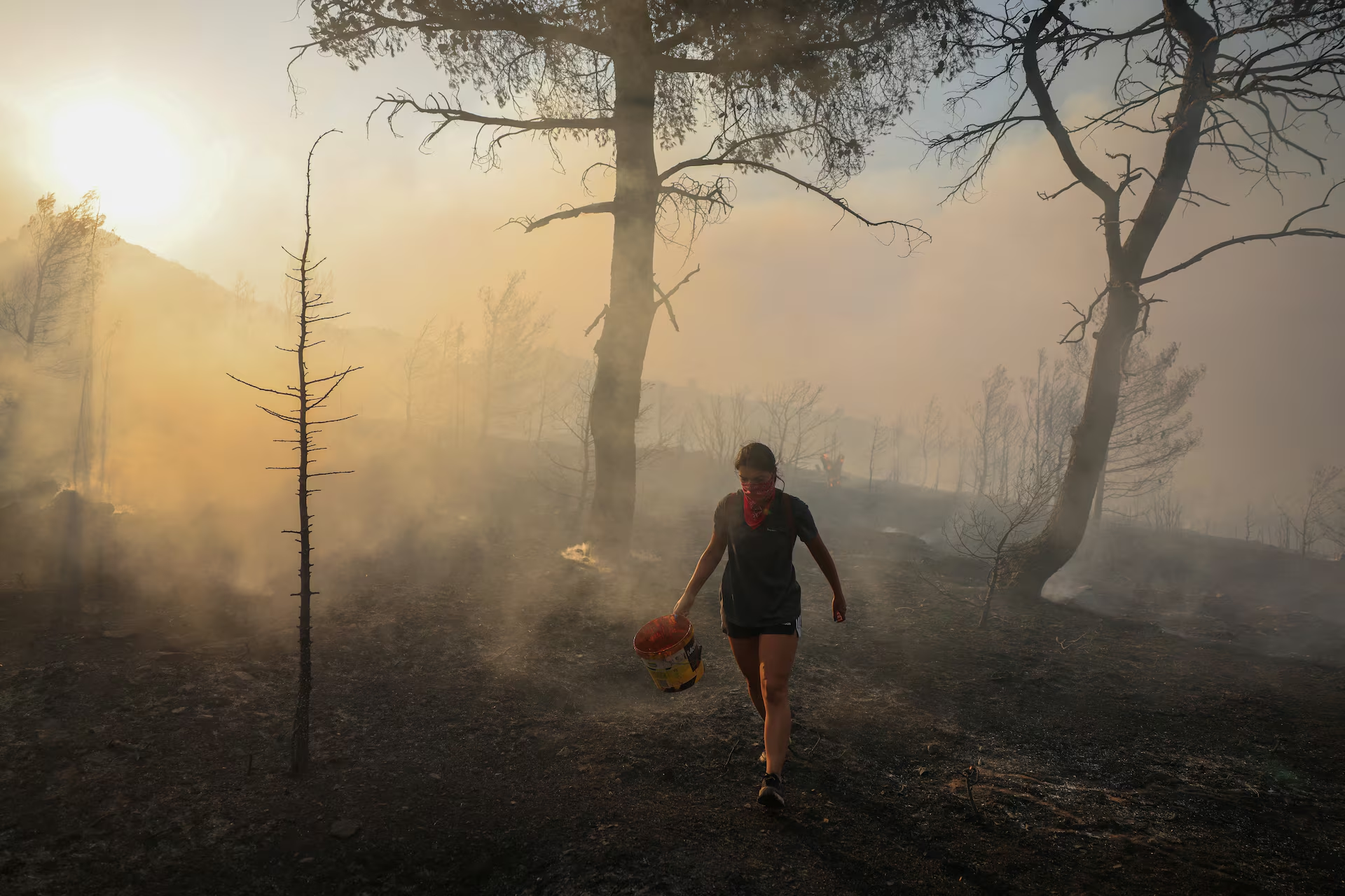 Marina Kalogerakou, 24, carries a bucket, as a wildfire burns in Penteli, Greece, 12 August 2024. Photo: Stelios Misinas / REUTERS