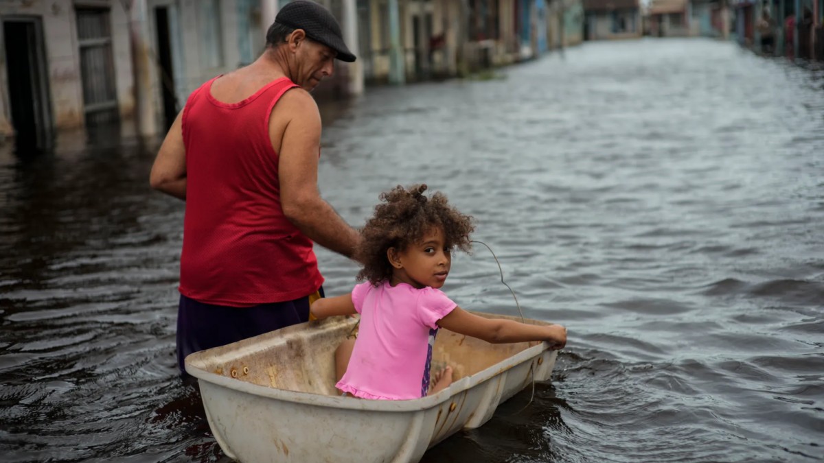 Jesus Hernandez guides his granddaughter Angelina via a container through a street flooded in the passing of Hurricane Helene, in Batabano, Mayabeque province, Cuba, on Thursday, 26 September 2024. Photo: Ramon Espinosa / AP Photo